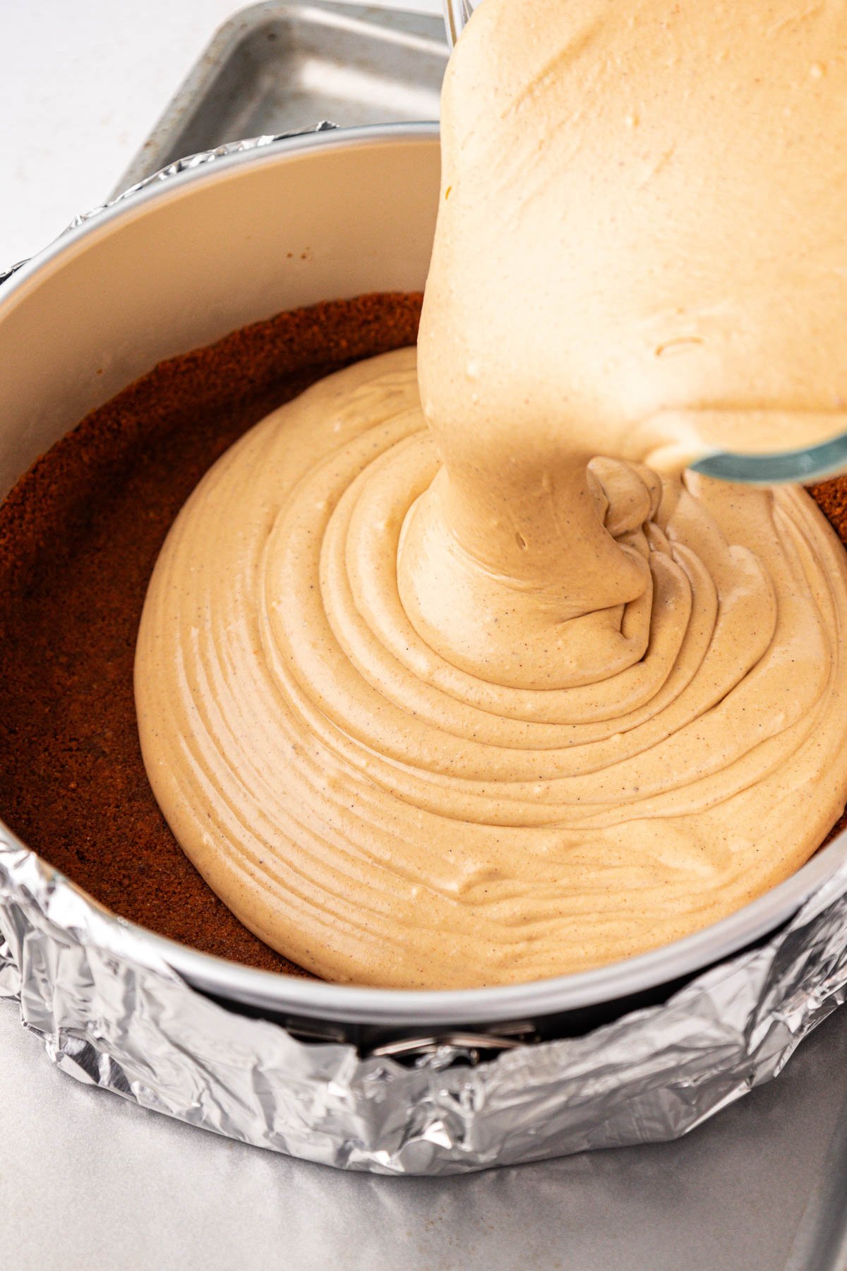 Cheesecake filling with spices being poured into a prepared crust in a pan.