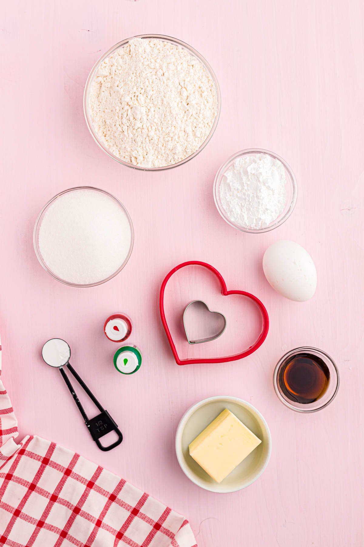 Overhead photo of ingredients to make sugar cookies on a pink surface. 