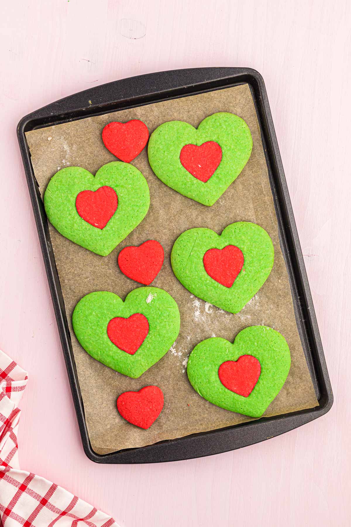 Heart shaped Grinch cookies on a baking sheet.