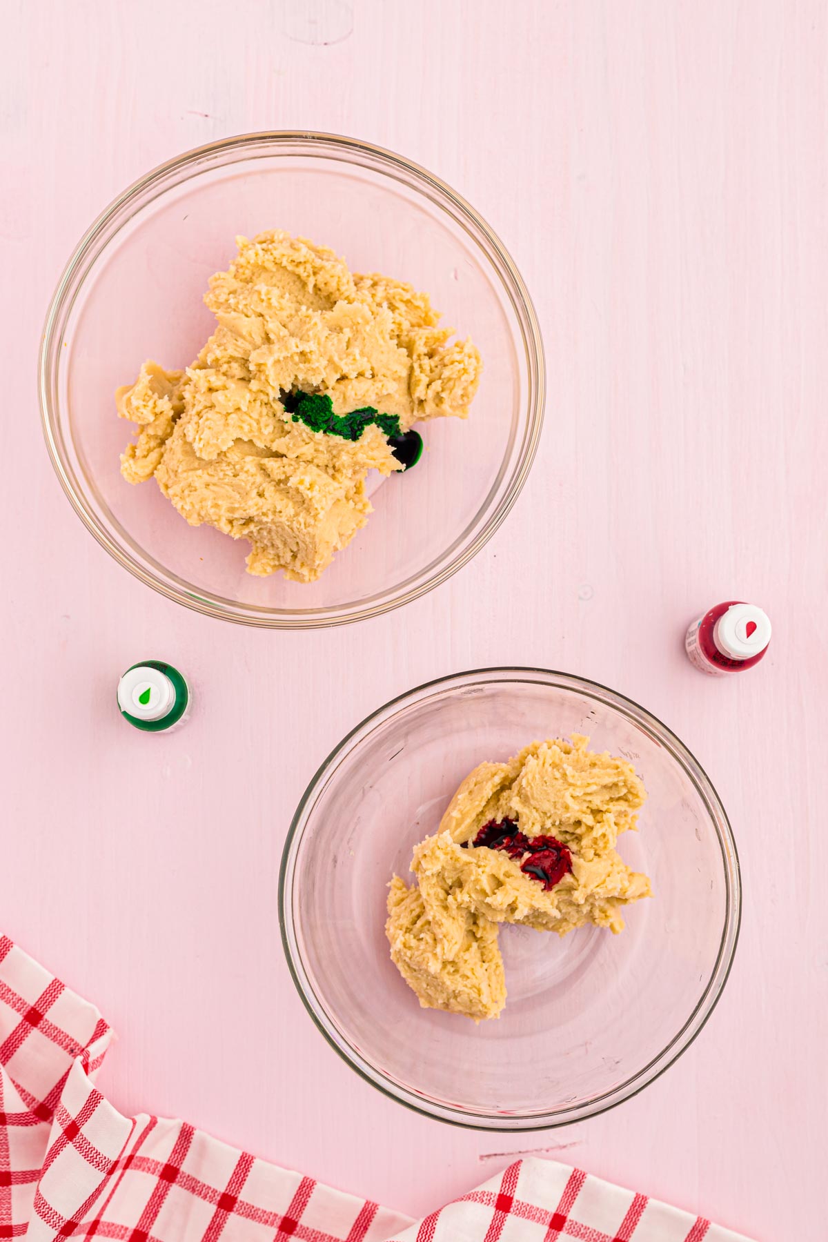 Sugar cookie dough in two glass mixing bowls getting food coloring added to them.