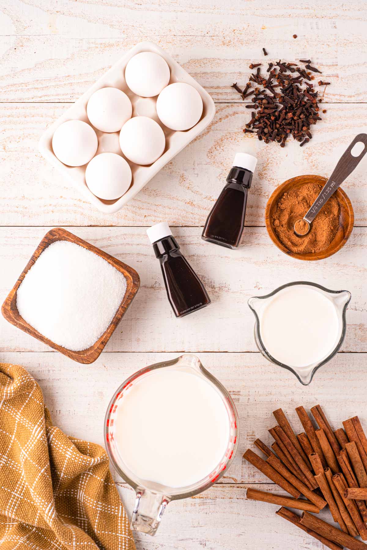 Overhead photo of the ingredients to make homemade eggnog on a light wooden surface.