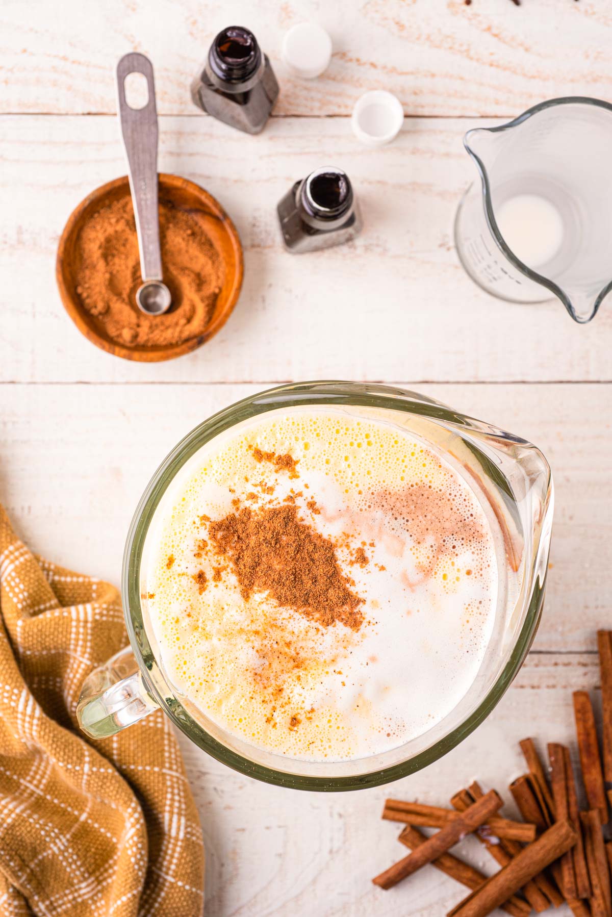 Eggnog being made in a large pitcher, spices are still sitting on top of the liquid mixture ready to be stirred in.