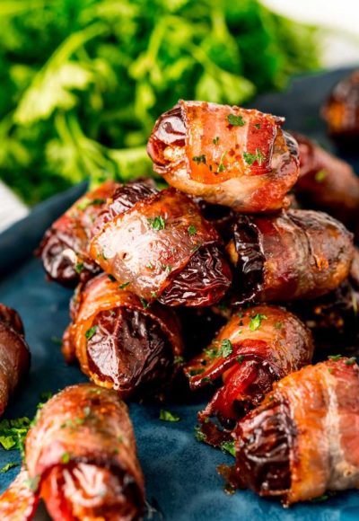 Close up photo of bacon wrapped dates piled on top of each other on a blue plate.