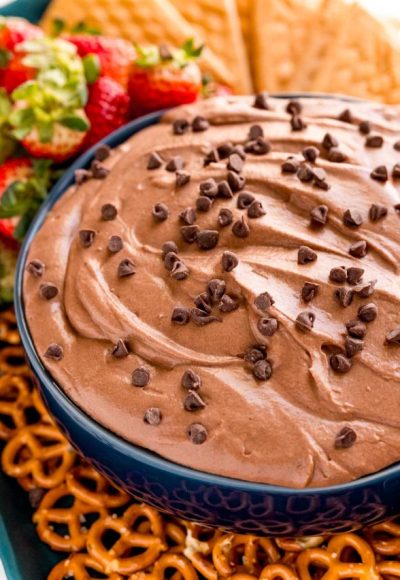 Close up photo of a blue bowl with brownie batter dip in it with pretzels, strawberries and cookies around it.