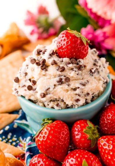 Close up photo of a teal bowl filled with cannoli dip surrounded by crackers and strawberries.