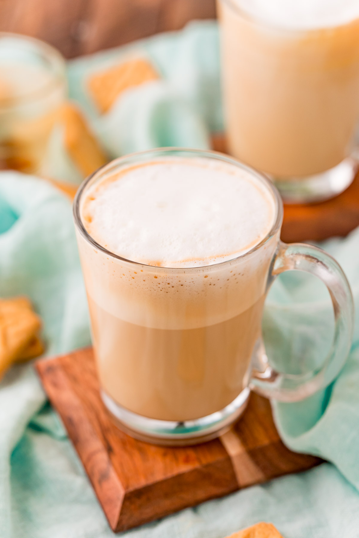 Close up photo of a breve latte in a clear glass mug on a wood coaster.