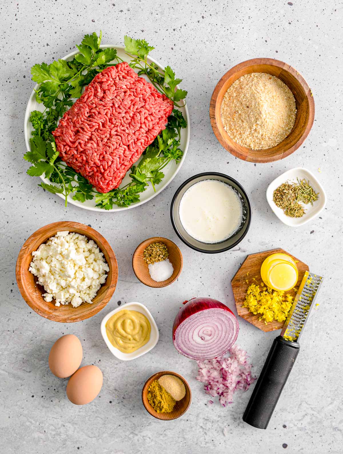 Ingredients to make Greek meatballs arranges on a gray counter.