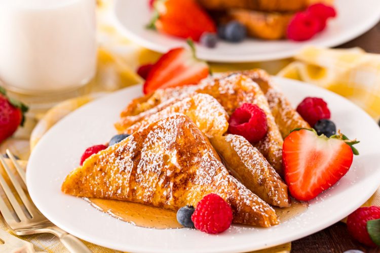 Close up photo of French toast on a white plate with berries.