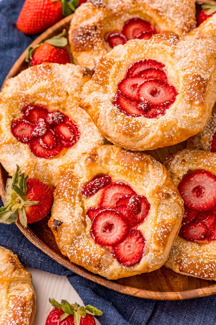 Close up photo of strawberry danishes on a wooden plate on a blue napkin.