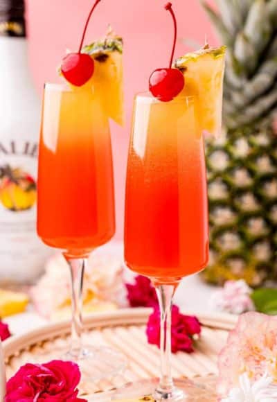 Close up photo of two Hawaiian Mimosas in champagne sluted garnished with pineapple wedges and cherries.