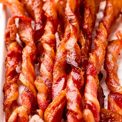 Close up photo of twisted bacon on a white serving tray.