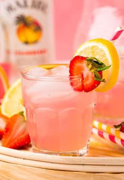 Close up photo of a small glass filled with a pink lemonade vodka cocktail on a rattan tray.