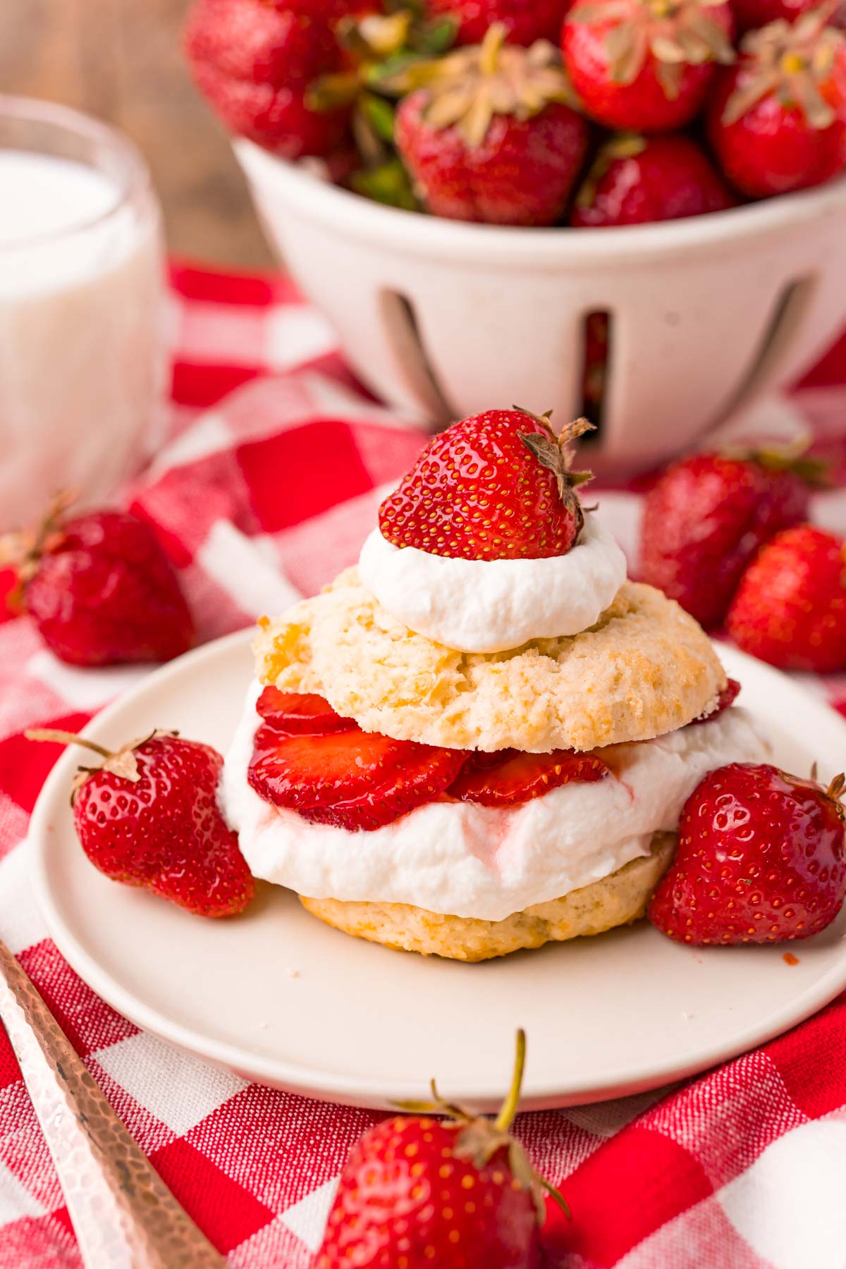 Strawberry shortcake on a tan plate on a red and white checkered napkin.