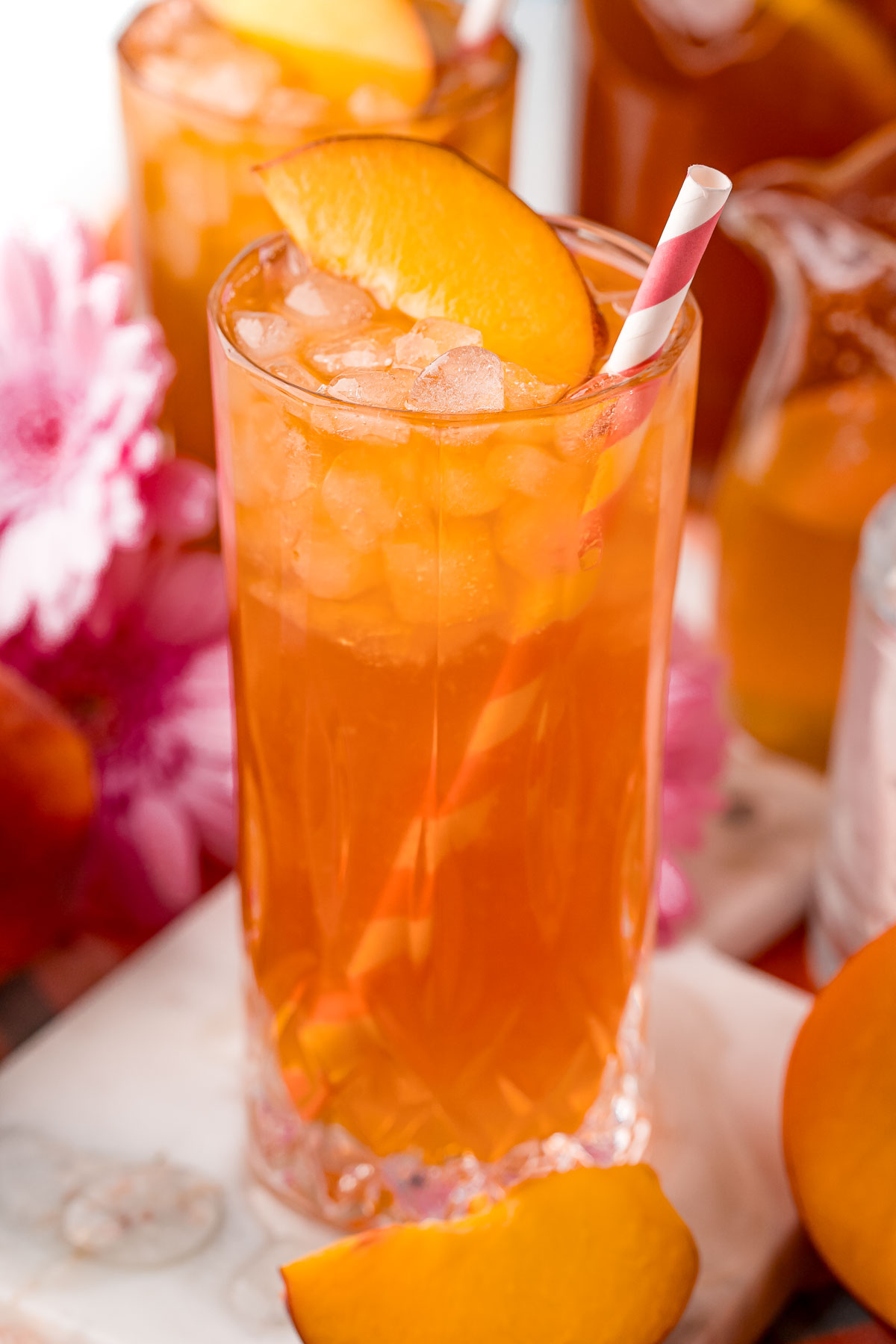 Close up photo of a glass with iced peach tea in it with another glass in the background.