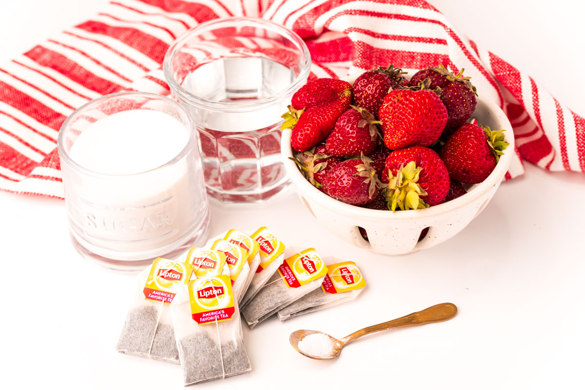 ingredients used to make strawberry sweet tea on a white table with a white and red striped napkin.