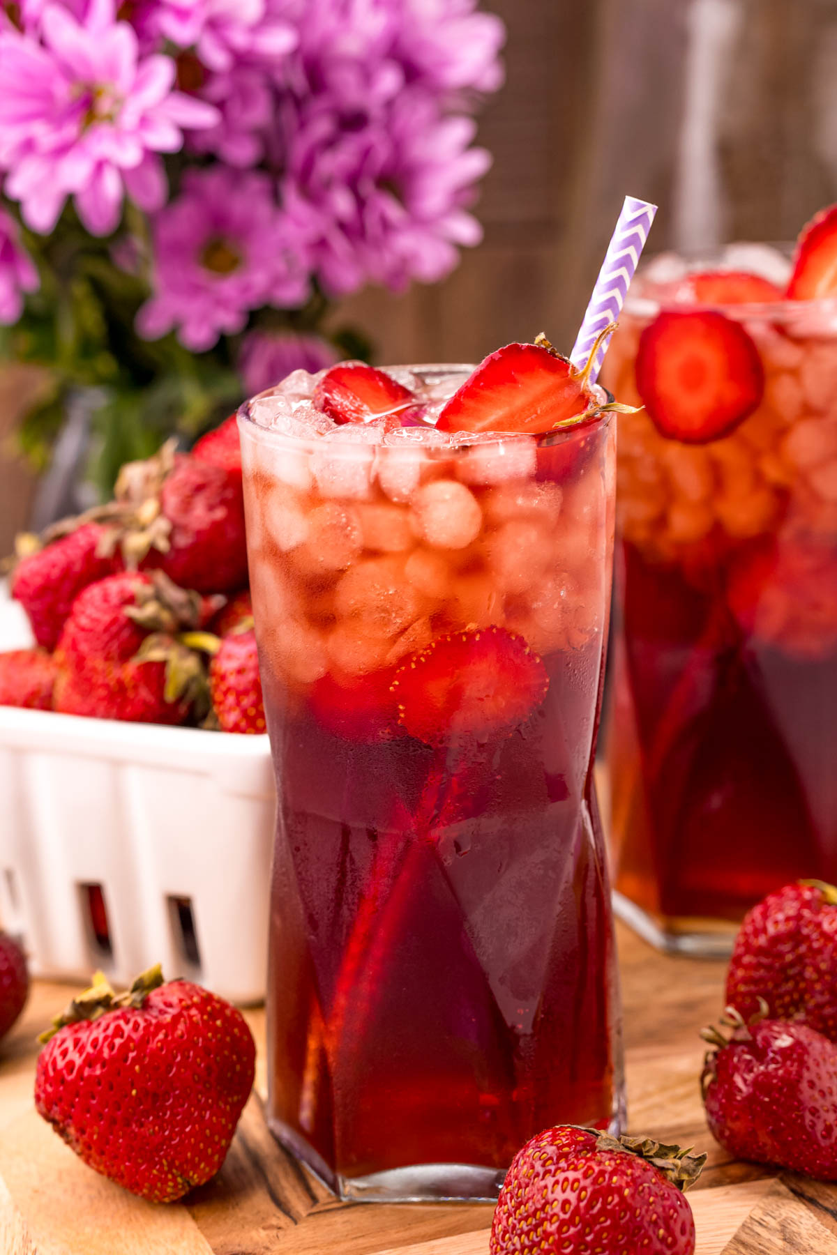 Close up photo of a glass of strawberry tea with another glass and a carton of strawberries in the background.