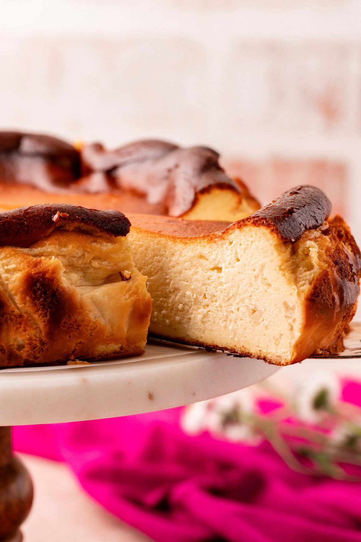 A slice of basque cheesecake being pulled from a cake stand.