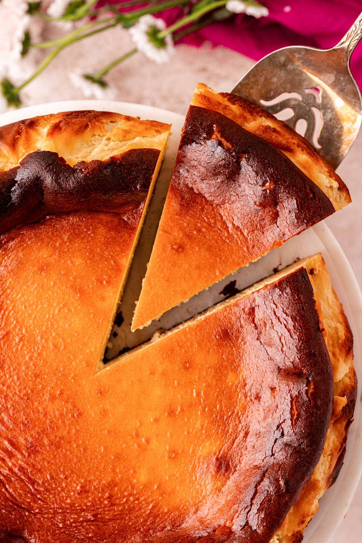 Overhead photo of a basque cheesecake with a slice being removed.