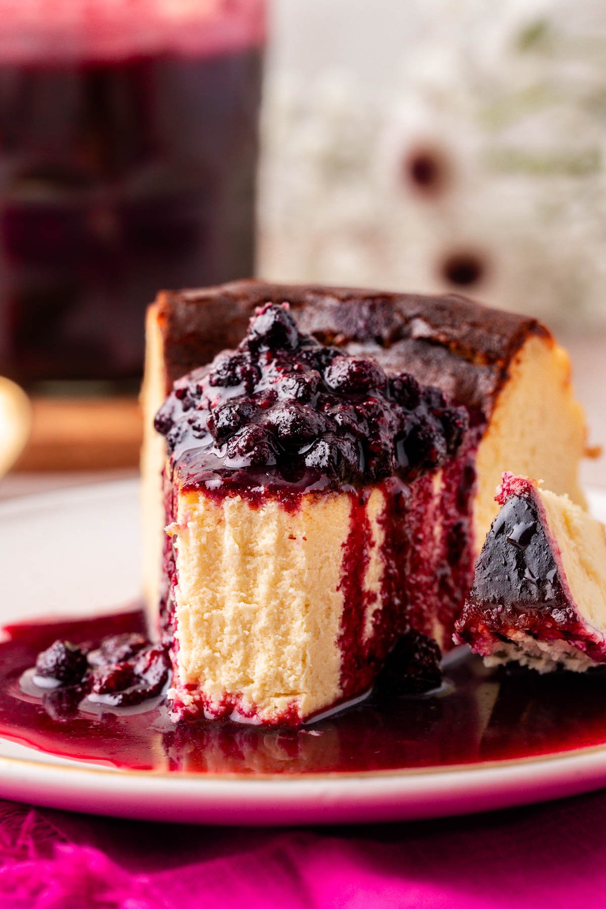 A piece of burnt cheesecake on a plate covered in berry compote.