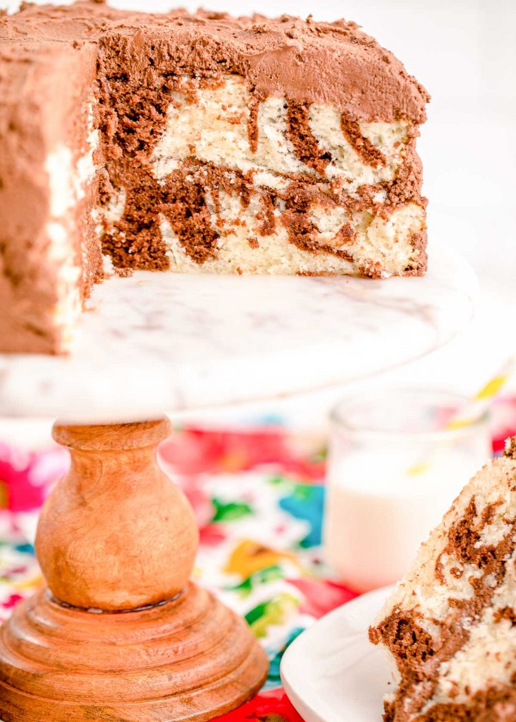 A marble cake with a slice taken out of it on a white marble cake stand.