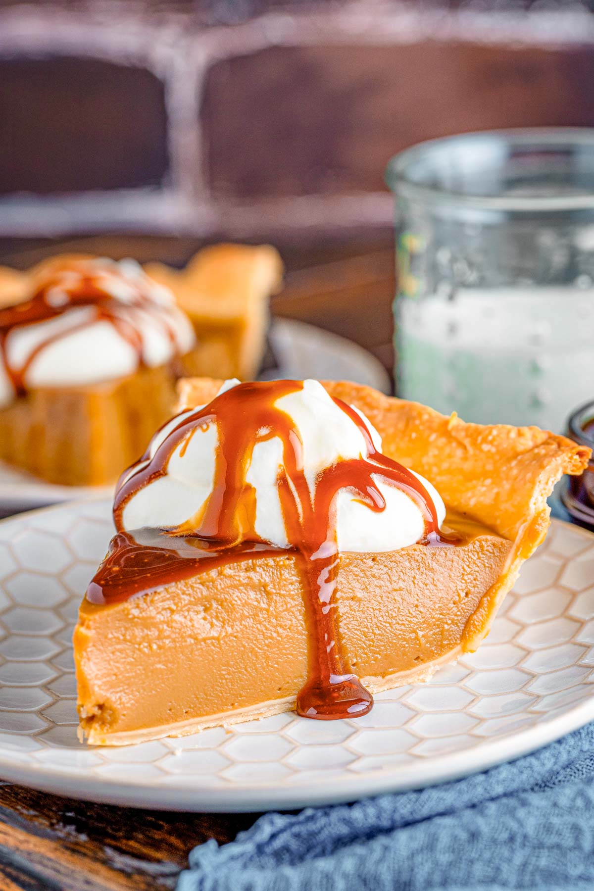 Close up photo of a slice of butterscotch pie on a white plate on a blue napkin.