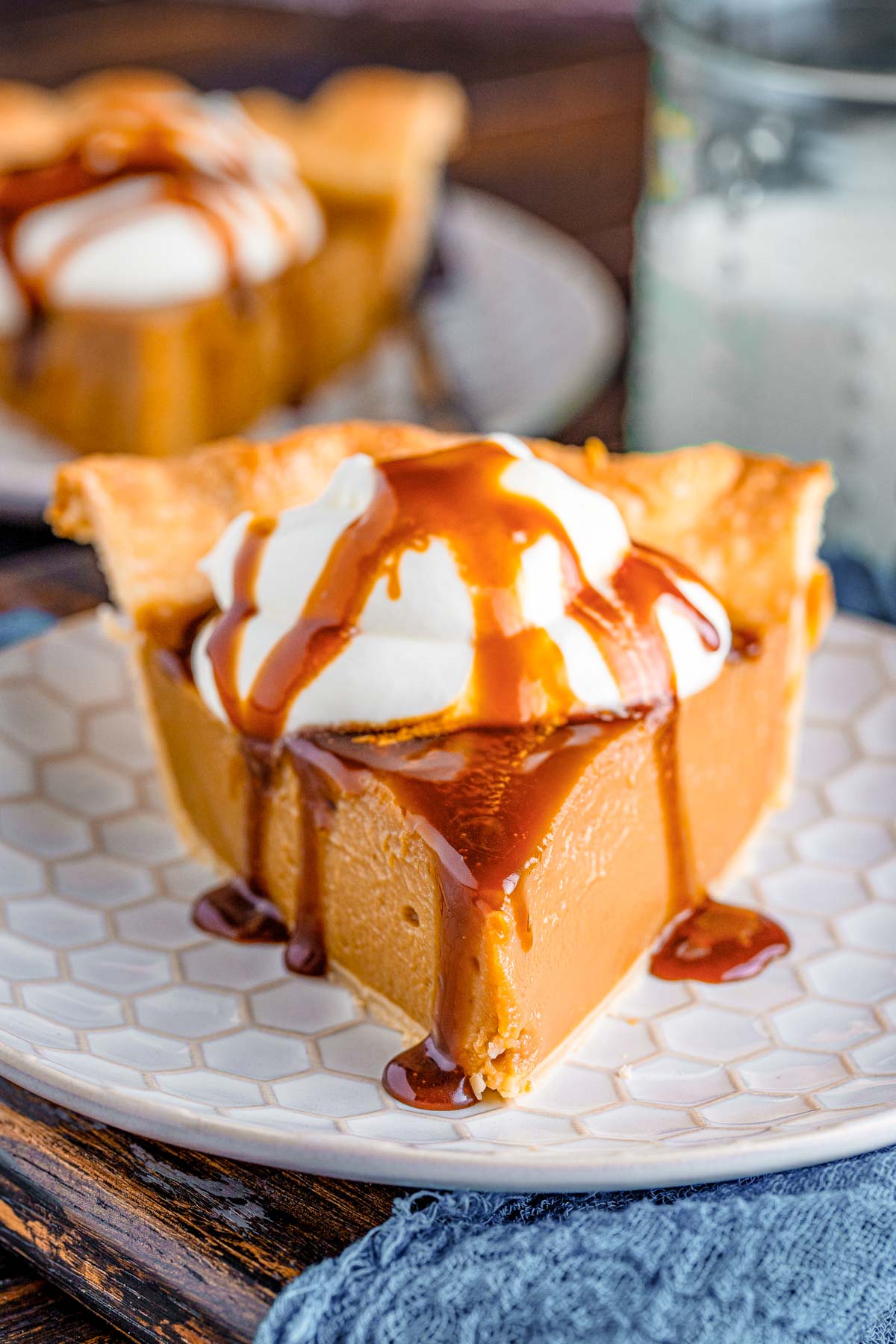 Close up photo of a slice of butterscotch pie on a white plate on a blue napkin.