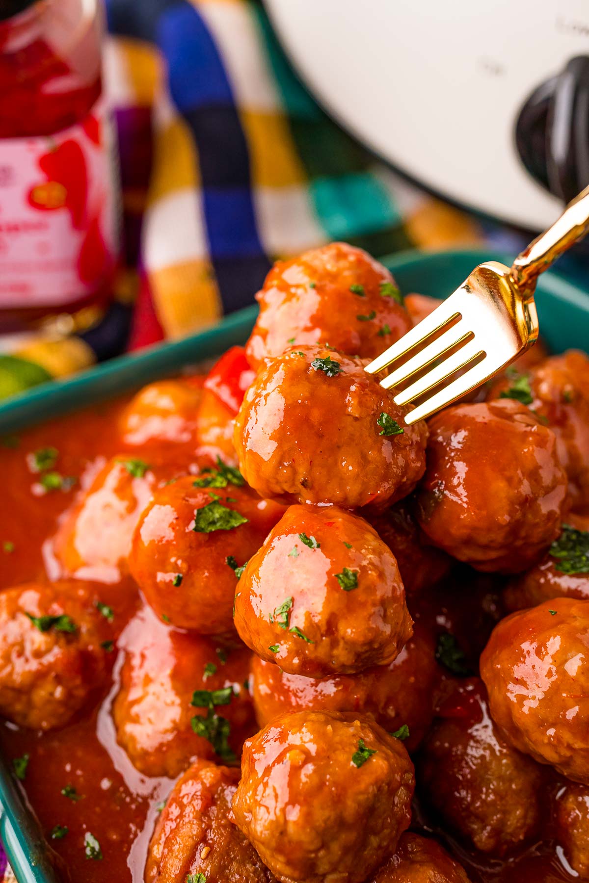 An appetizer fork taking a cocktail meatball off a plate of meatballs.