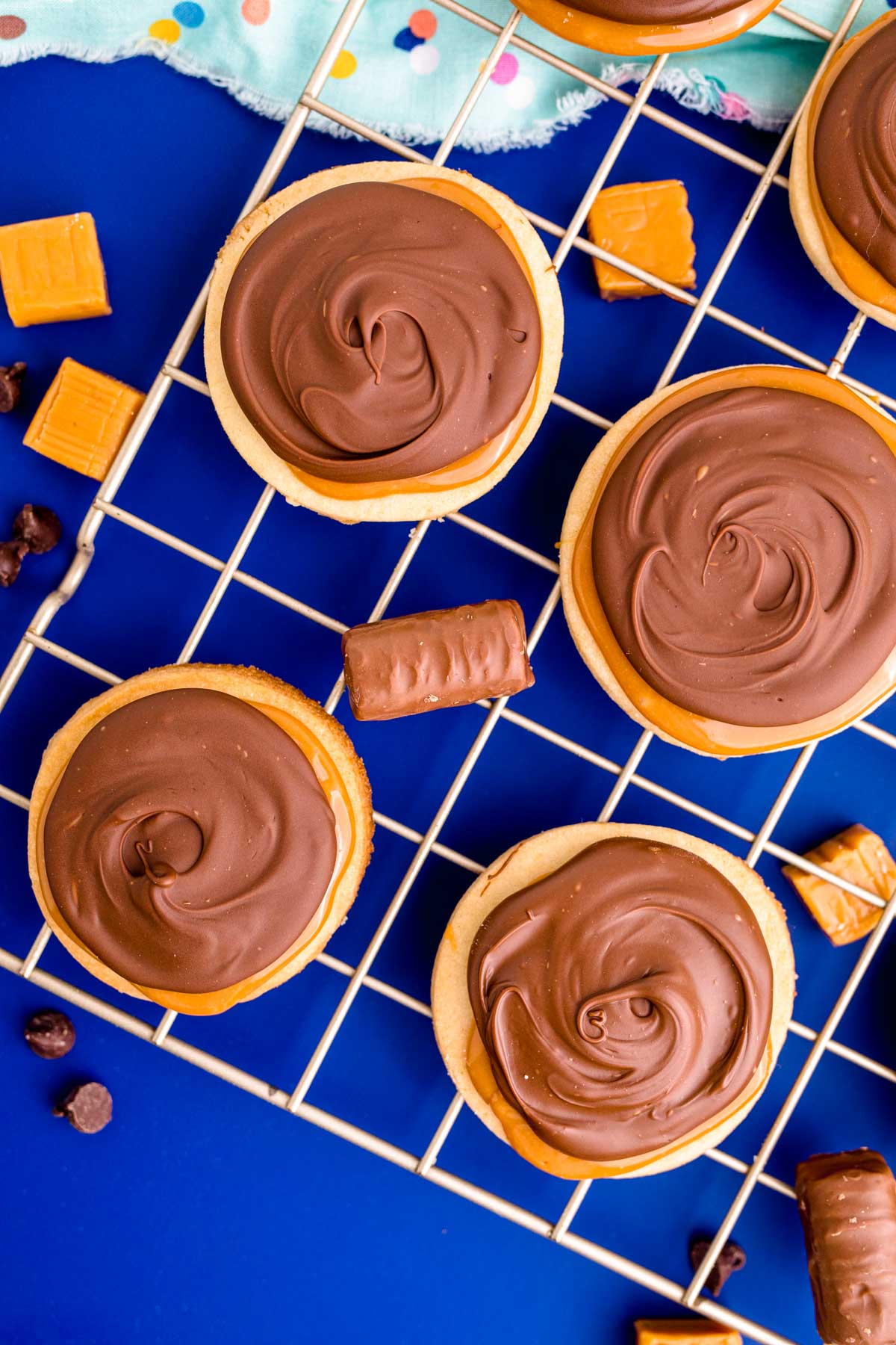 Overhead photo of twix cookies on a wire rack on a blue surface.