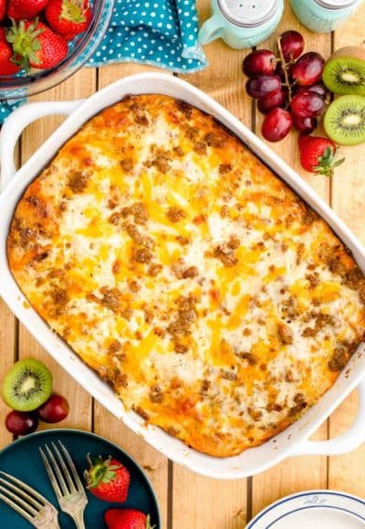 Overhead photo of a biscuits and gravy casserole on a wooden table with fruits and serving plates around it.