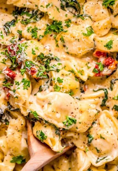 Close up photo of a wooden spoon in a pot of tortellini alla panna.