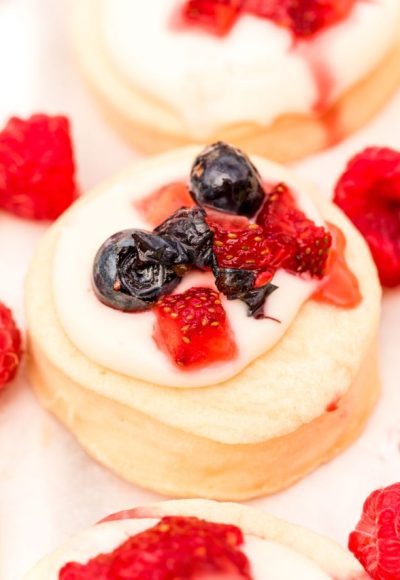 Close up photo of shortcake cookies topped with cream cheese frosting and berries.