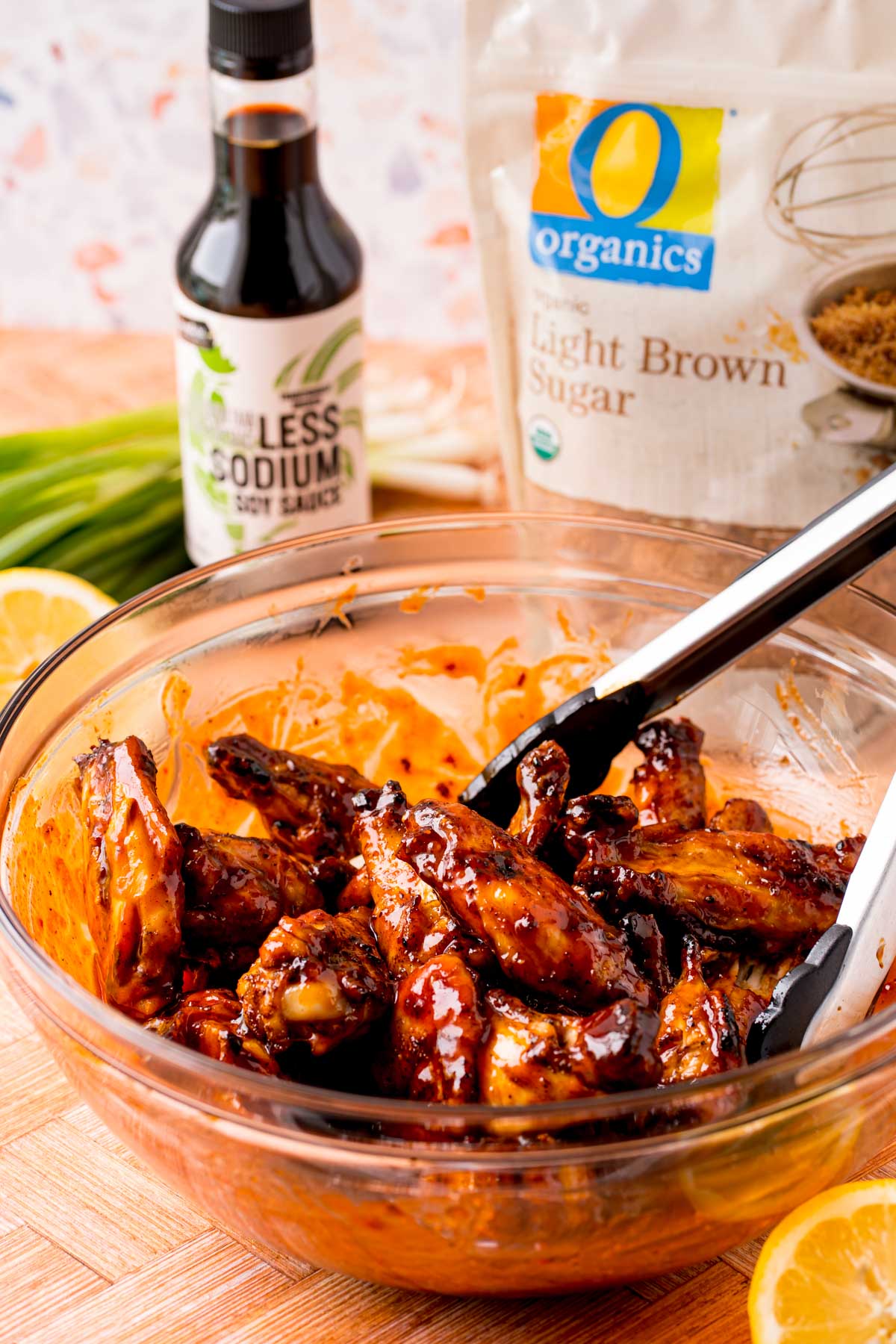 Wings being tossed in Korean BBQ sauce in a glass bowl.