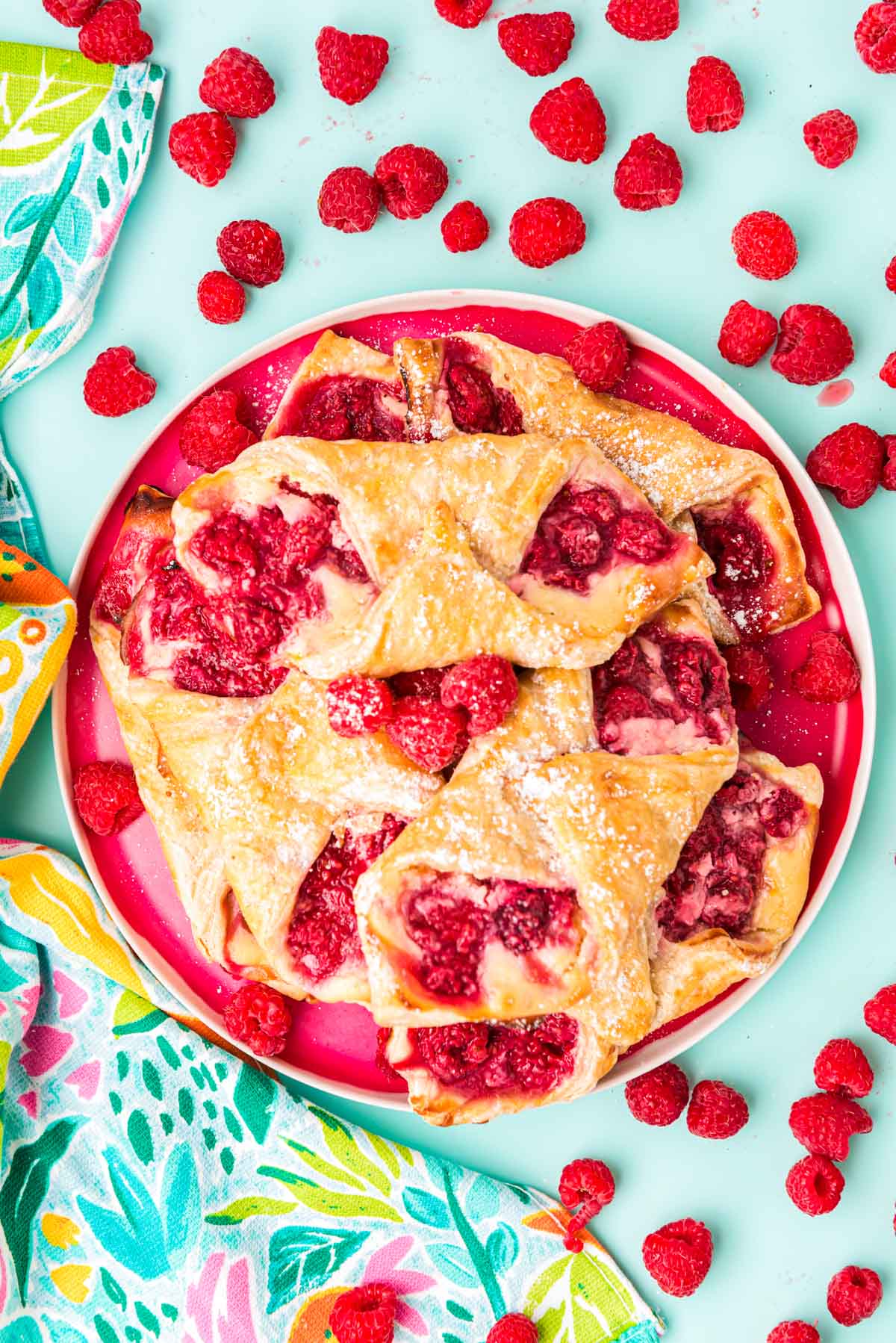 Overhead photo of raspberry danishes on a plate on a blue surface.