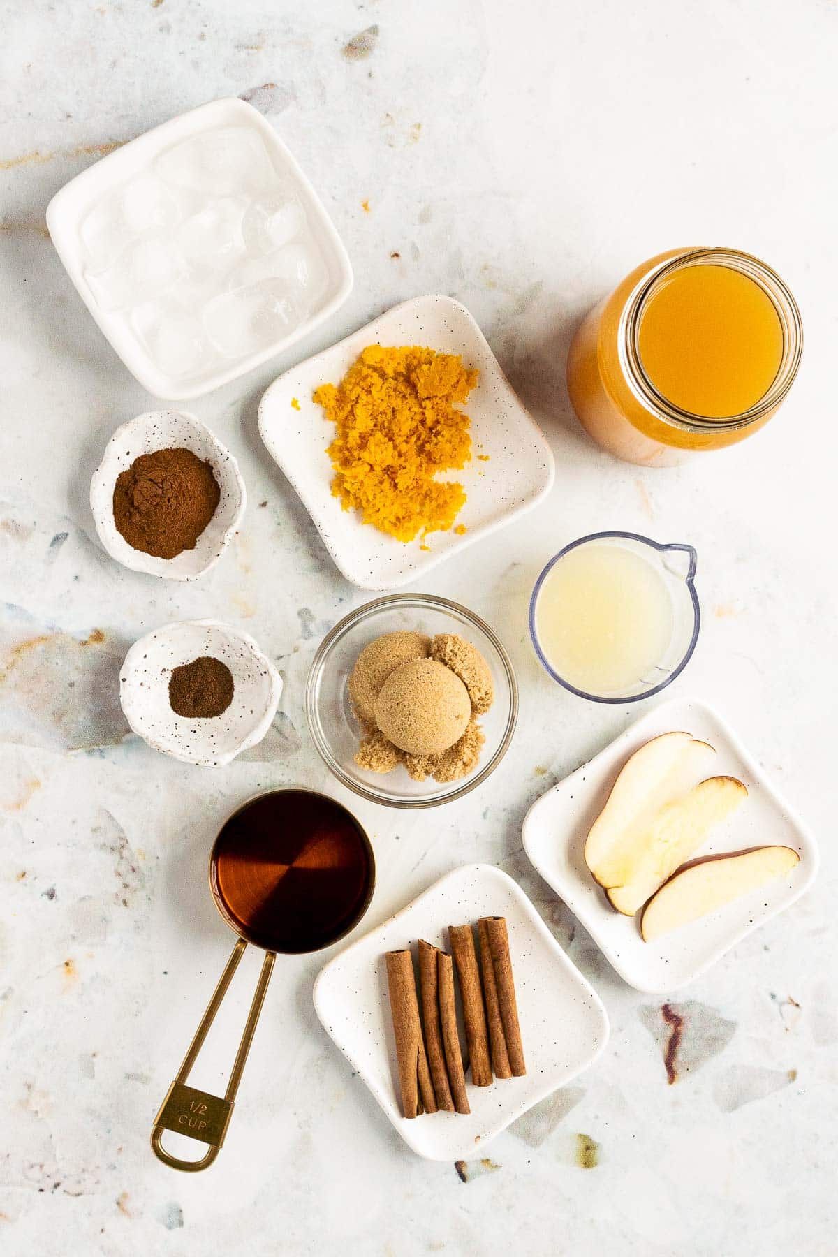 Ingredients to make apple cider bourbon cocktail prepped on a marble counter.