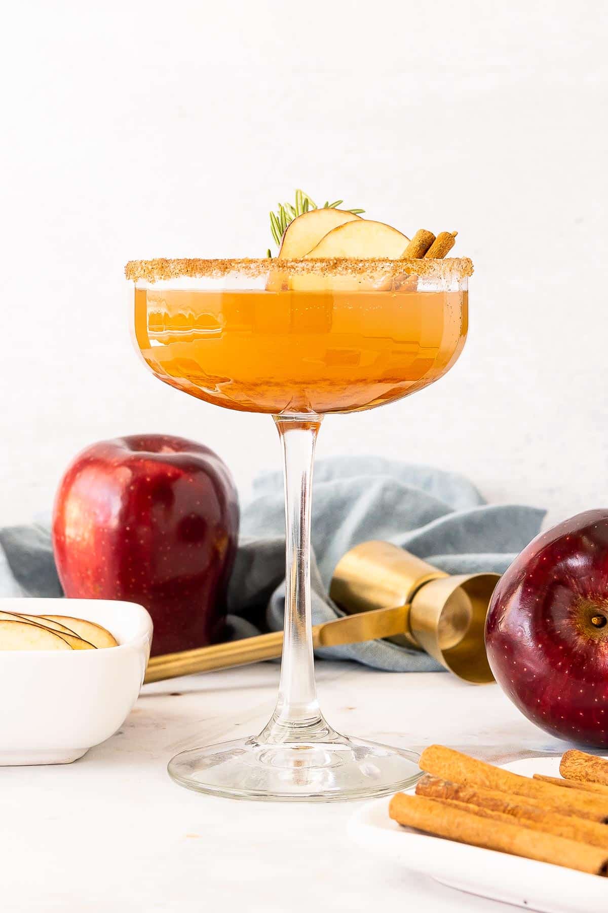 A coupe glass filled with an apple cider bourbon cocktail on a white marble surface.