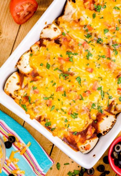 Overhead photo of chicken enchiladas in a baking dish on a wooden table.