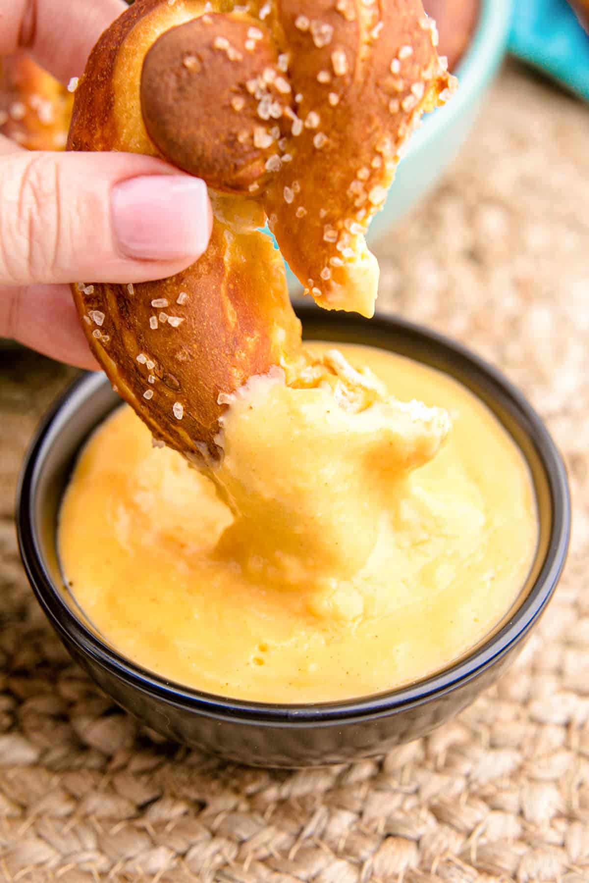 A woman's hand dipping a soft pretzel in beer cheese dip.