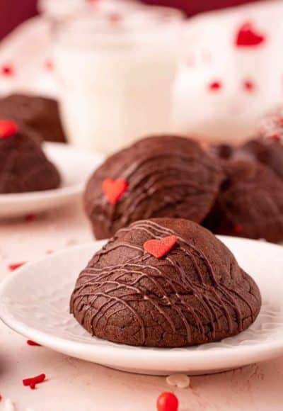 Chocolate cookies on a white plate with more cookies behind it.