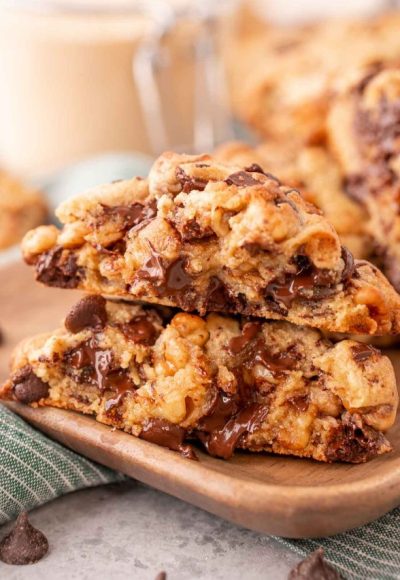 A Levain chocolate chip cookie has been broken in half and the halves are stacked on top of each other on a wooden plate.