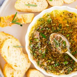 Overhead photo of slices baguette on a white plate with a dish of dipping oil and herbs.