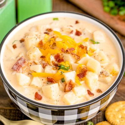 A close up photo of a white and black checkered bowl filled with potato soup on a wooden table.