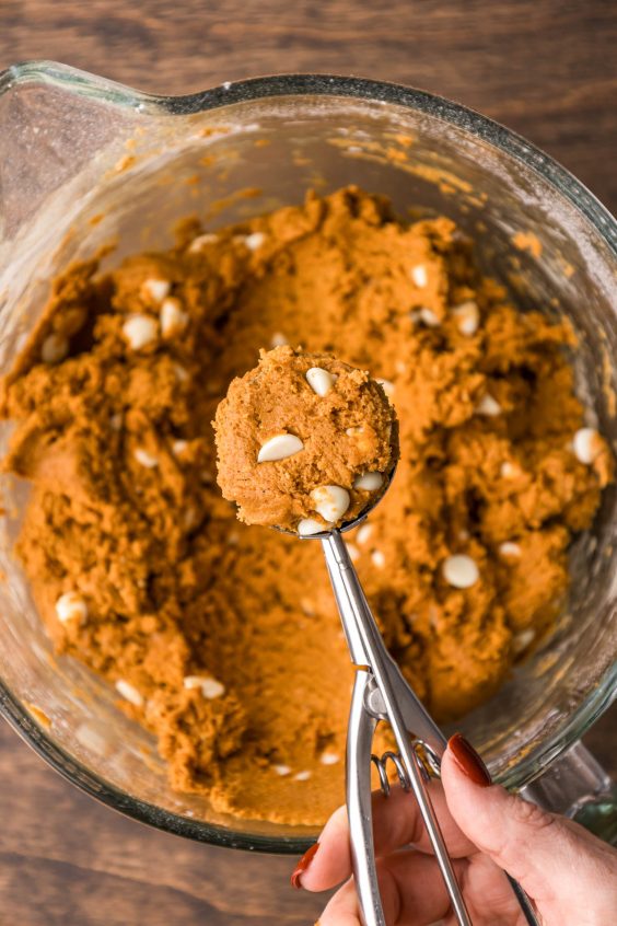 A cookie scoop scooping dough out of a glass bowl.