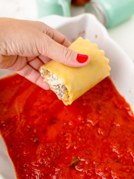 A lasagna roll up being places in a pan.