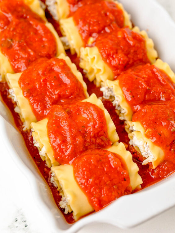 Marinara sauce on top of lasagna roll ups ready to bake.