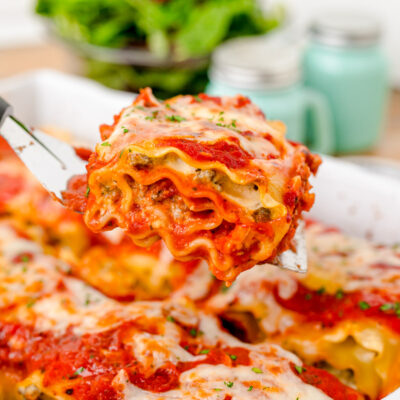 Close up of a spatula scooping a lasagna roll-up out of a pan.