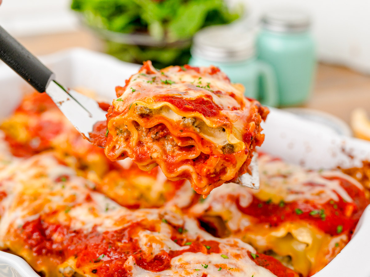 Close up of a spatula scooping a lasagna roll-up out of a pan.