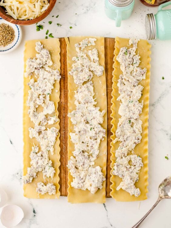 Three lasagna noodles with ricotta filling spread over them on a cutting board.