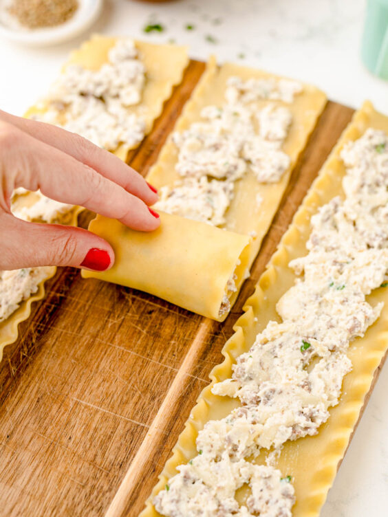 A woman's hand rolling lasagna noodles.