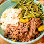 Mississippi pot roast served in a teal bowl with potatoes and green beans.