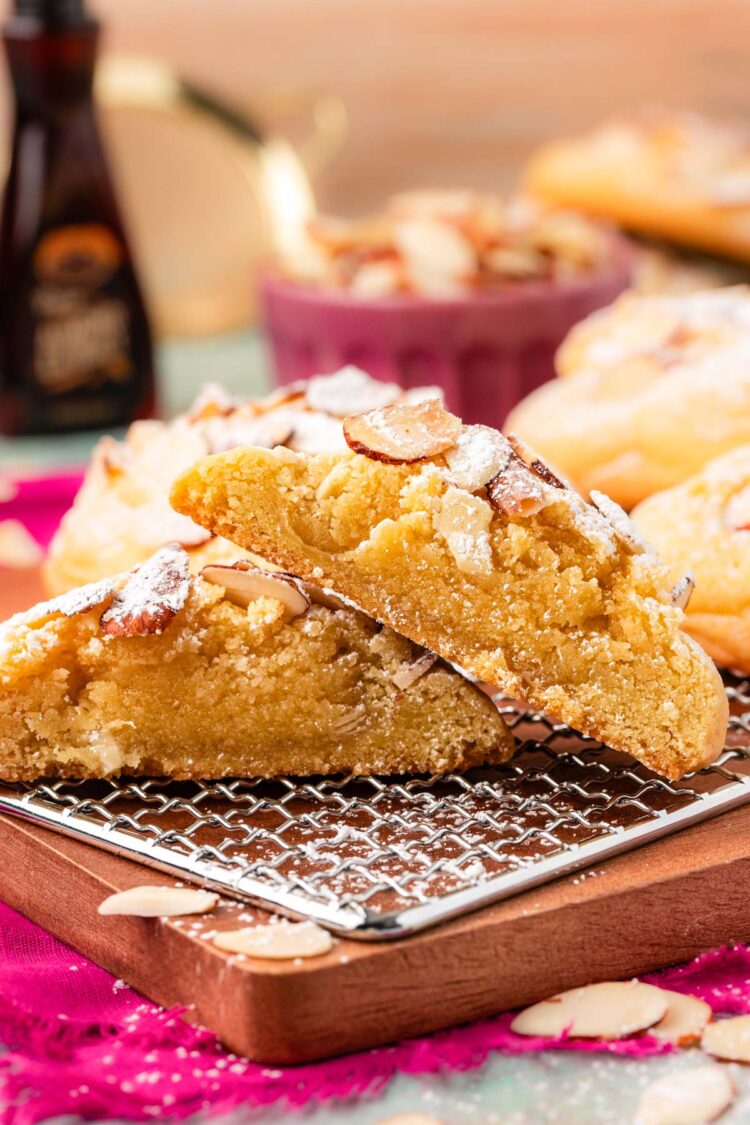 Almond croissant cookies on a serving board, one has been sliced in half to show the frangipane filling.